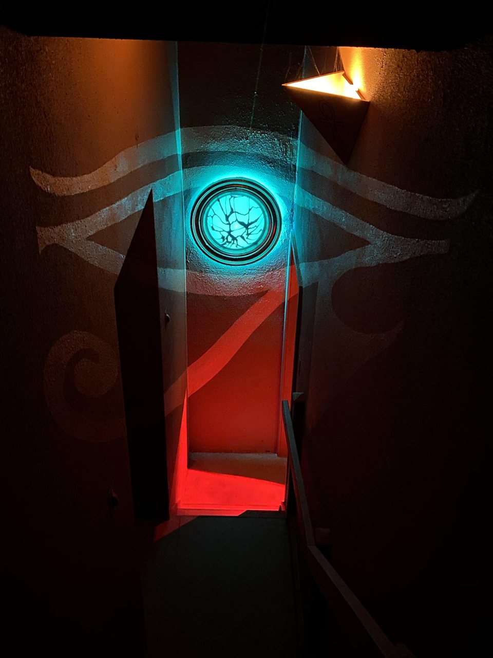 Egyptian eye mural with a glowing turquoise disc above a red-lit passage