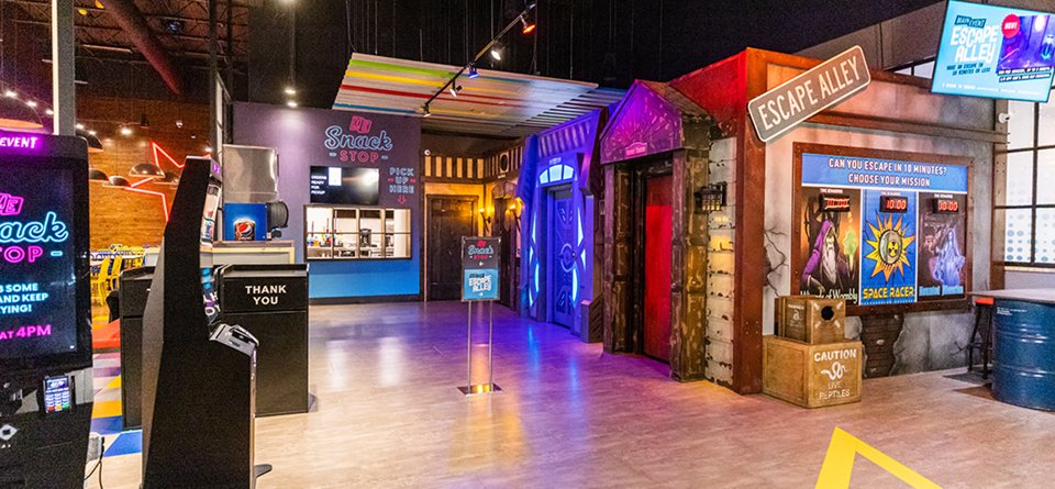 Az Escape Alley folyosó tematikus szobabejáratokkal, küldetéstáblával és büfépulttal