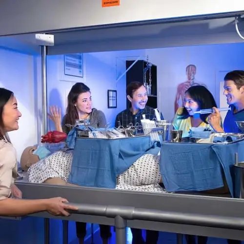 A team in a hospital ward set where a patient dummy lies on a bed covered with instruments