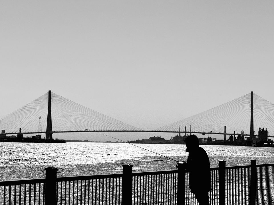 An angler on the shore, the bridge behind