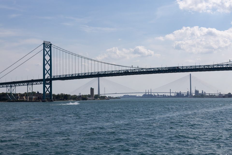 The Ambassador Bridge from the river, the Gordie Howe framed beneath it, 2025