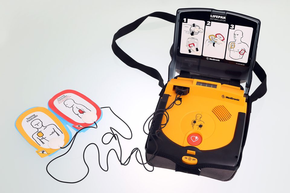 An open AED with its two pads; drawings on the lid show the steps