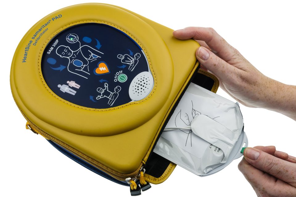 A hand pulls the pad pack out of a yellow AED