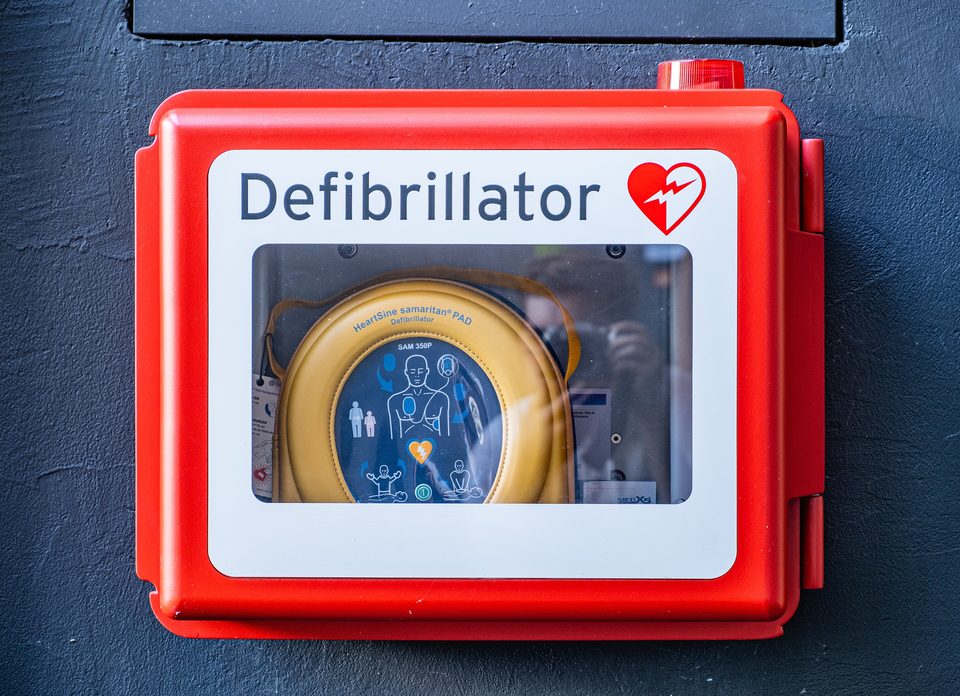 A red wall cabinet holding an AED, marked with a heart and the word Defibrillator