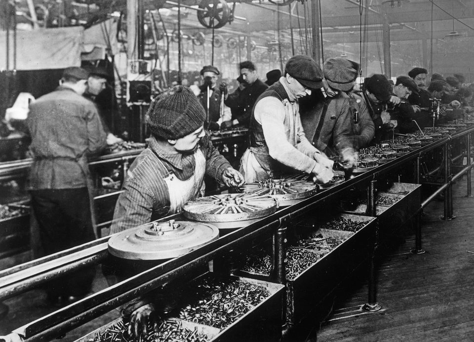 Workers on Ford’s first moving assembly line at Highland Park put together magnetos and flywheels (1913)