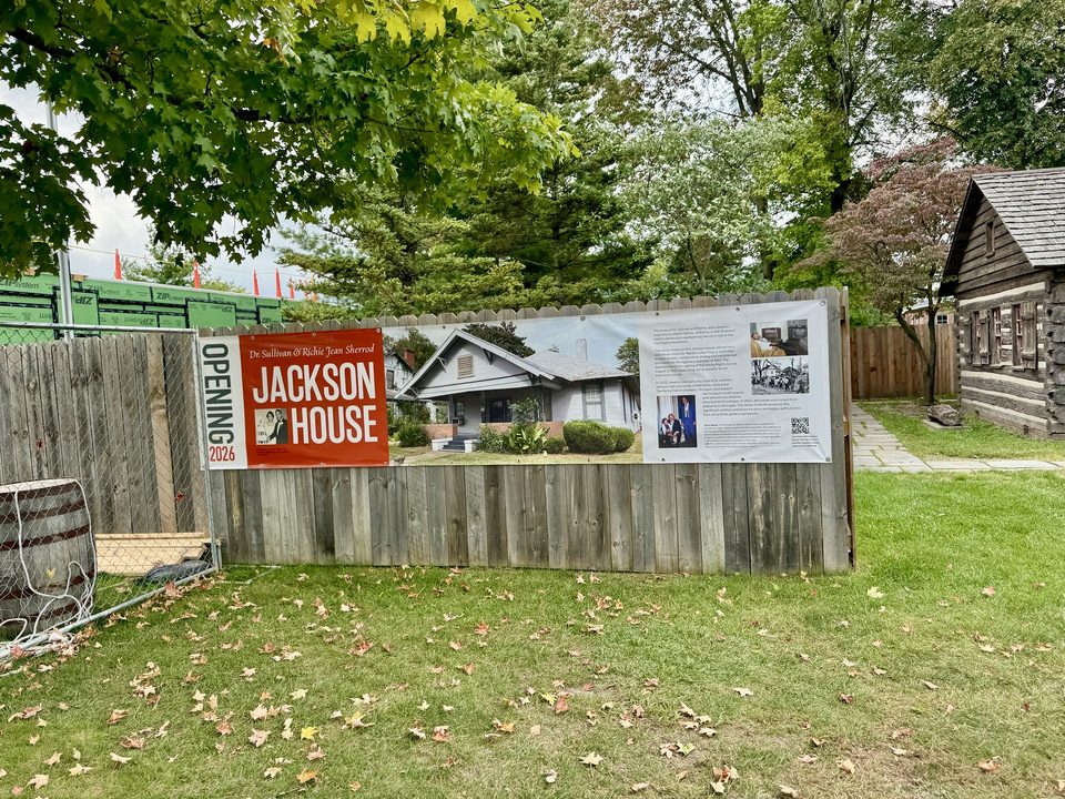 The Jackson Home construction site in Greenfield Village, September 2024, with a fence banner showing the house in Selma and announcing its 2026 opening