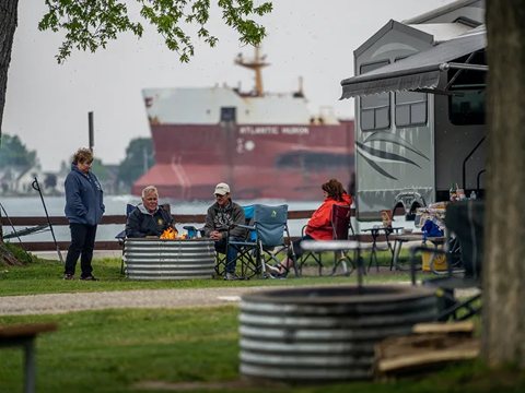 Kempingezők tűzrakó hely mellett, mögöttük elhaladó teherhajó