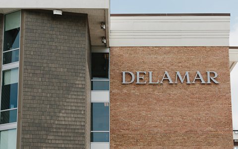 A szálloda téglahomlokzata a DELAMAR felirattal és a mellette álló zsindelyburkolatú szárny