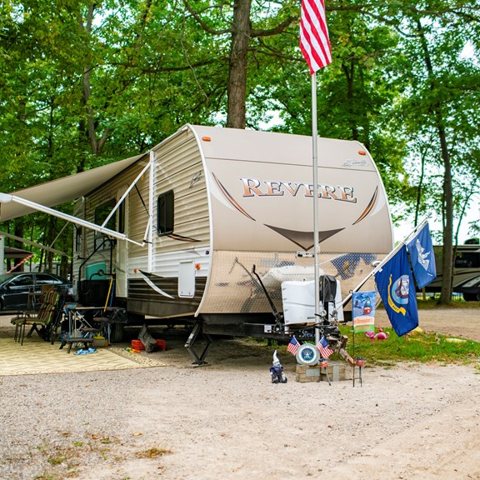 A trailer with an awning and flag under trees