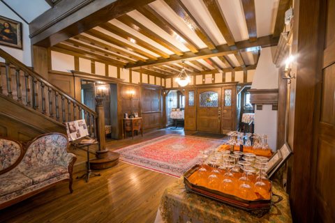 The wood-paneled entrance hall with a beamed ceiling, a staircase and a Persian rug