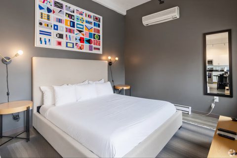 A bedroom with a large bed and gray walls beneath a colorful flag artwork