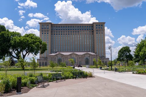 The Michigan Central Station facade seen from Roosevelt Park under a blue sky with puffy clouds