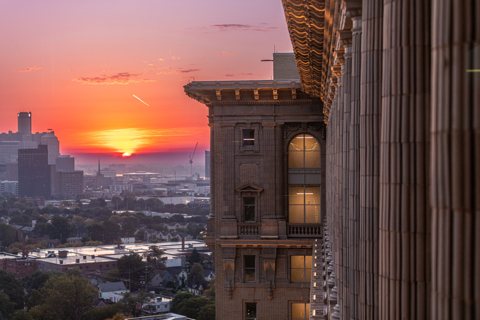 An orange sun over the city rooftops seen from the station's eighteenth floor, beside its ornate stone facade