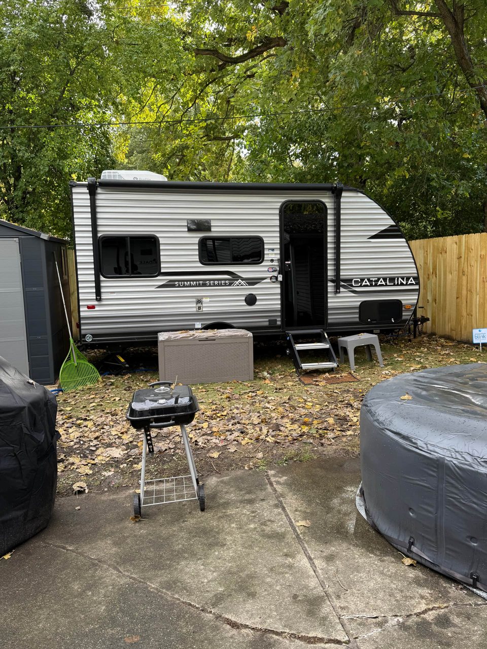 A travel trailer with a grill and hot tub beside the fence
