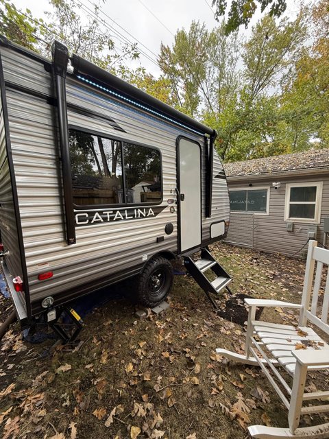 A travel trailer with steps and a chair beneath the trees
