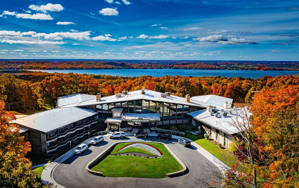 Aerial view of the Lakeview Hotel and its driveway, with autumn forest and the lake behind