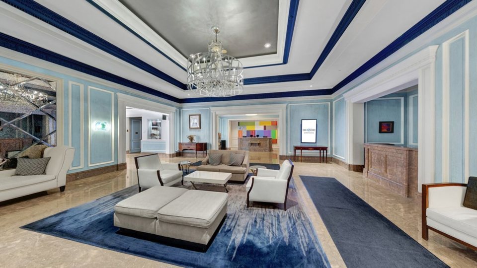 The lobby with a crystal chandelier, a blue rug and light-coloured seating