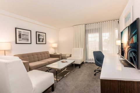 Suite living room with a sofa, white armchairs and large windows