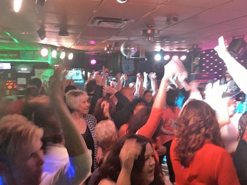 A dancing crowd with raised hands under colorful stage lights