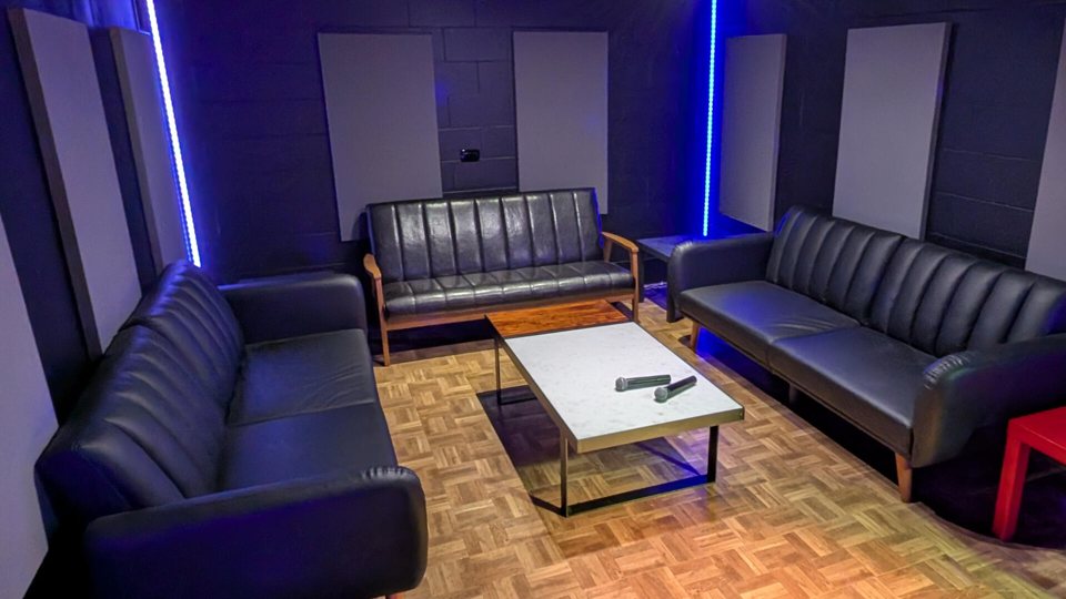 Karaokeszoba sötét bőrkanapékkal és alacsony asztallal, kék LED-csíkokkal