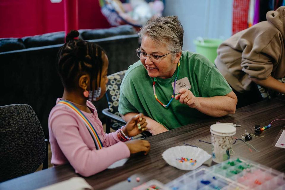 An older woman and a girl making beaded crafts at a family day
