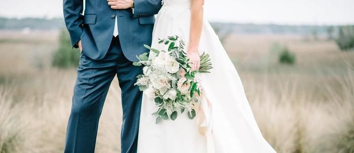 Bride holding a white rose bouquet with greenery beside the groom
