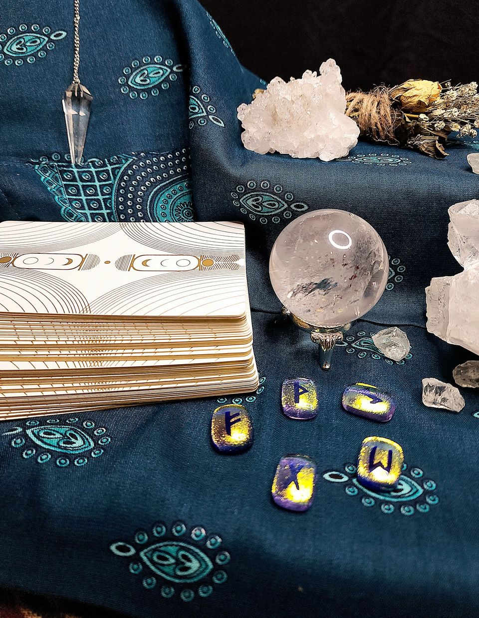 Crystal ball, rune stones and a pendulum on a teal cloth