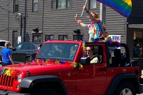 Rainbow-clad rider waving a flag atop a red Jeep in the Pride parade