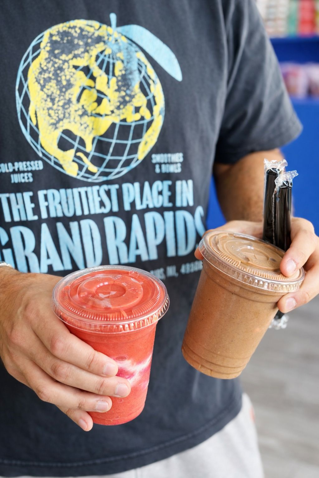 Two smoothies held in front of a 'The Fruitiest Place in Grand Rapids' T-shirt