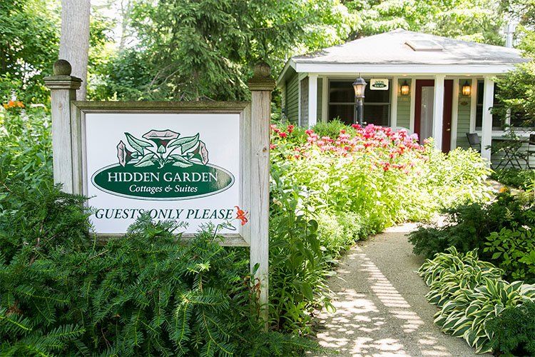 Hidden Garden Cottages & Suites sign in the garden with a cottage behind