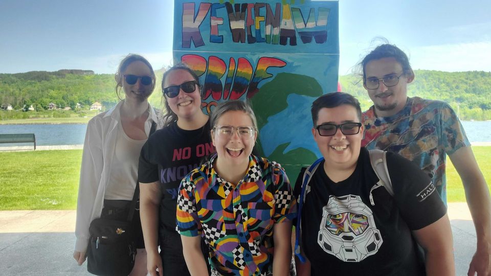 Friends posing in front of a painted Keweenaw Pride sign