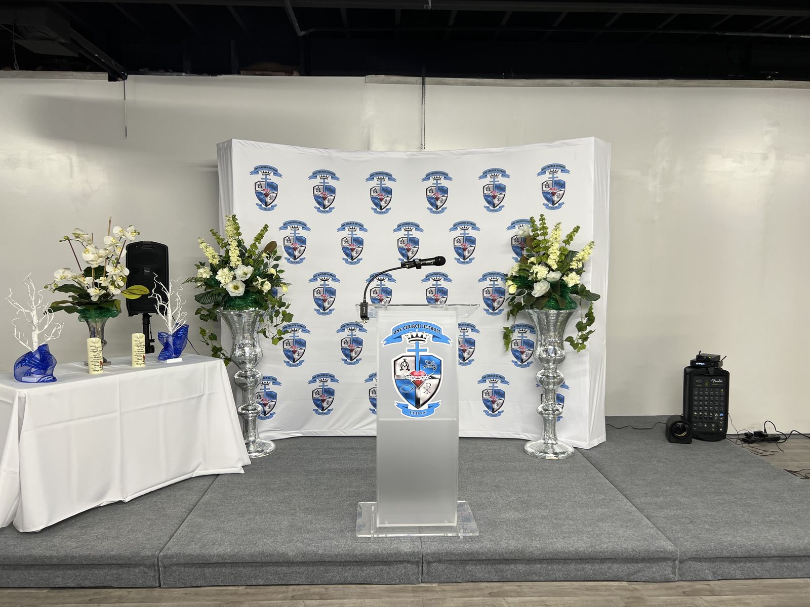 One Church Detroit's worship space with a lectern, flowers and logo backdrop