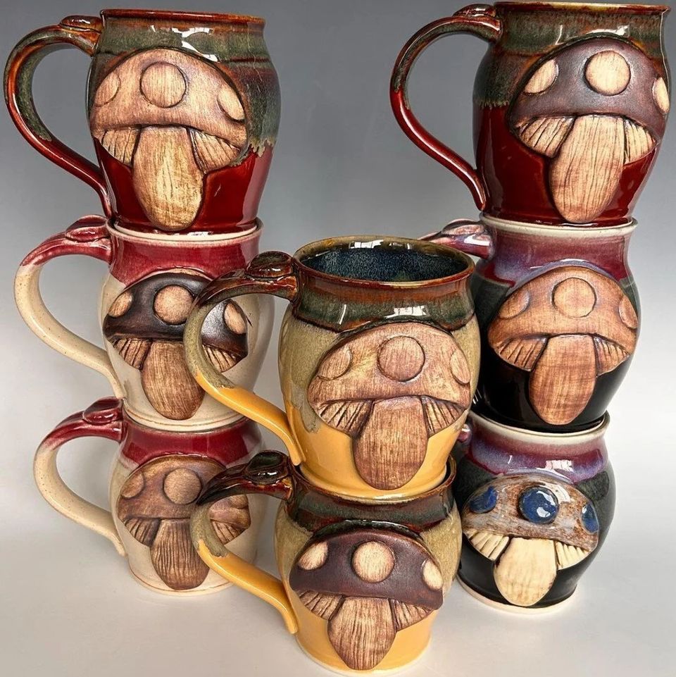 Stacked handmade ceramic mugs decorated with carved mushroom designs