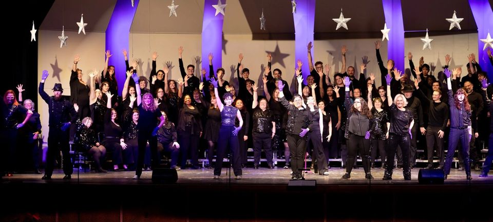 Chorus members sing with raised arms on a star-decorated stage