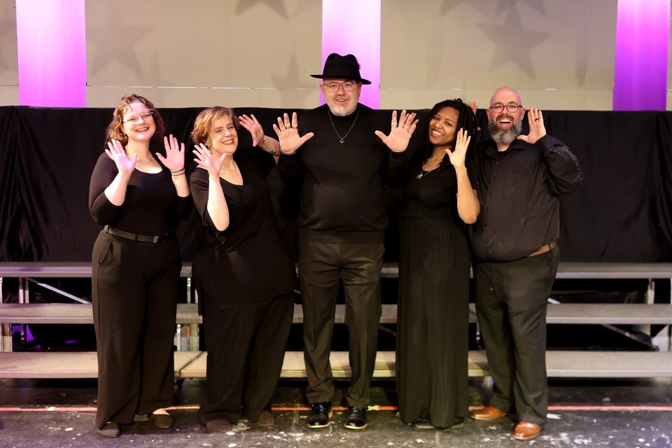 Five singers dressed in black wave from the stage