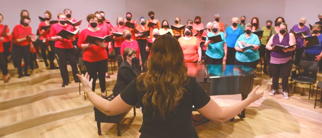 The chorus sings in colorful shirts as the director leads with outstretched arms
