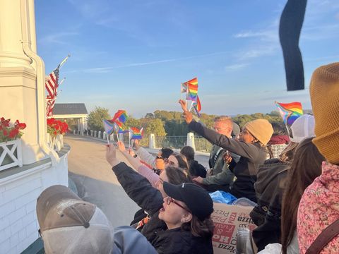 Revelers waving rainbow flags on a white-columned porch