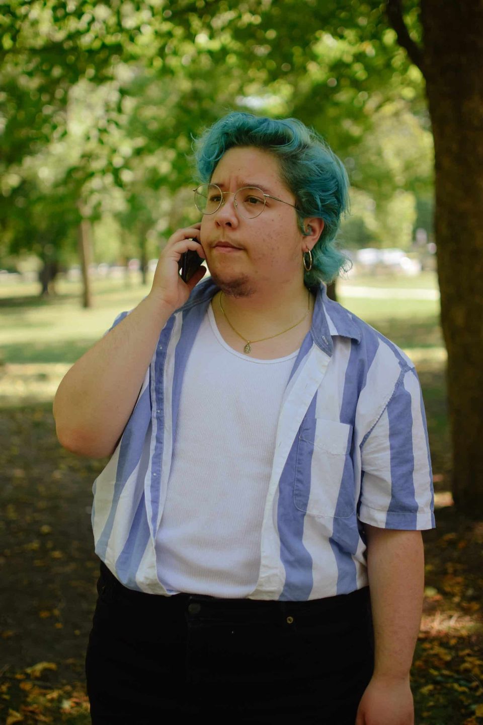 Person in a striped shirt talking on the phone under trees