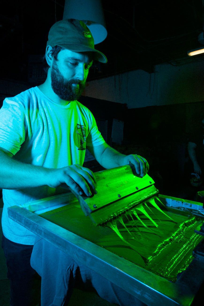 Screen printer pulling ink across a screen in green light