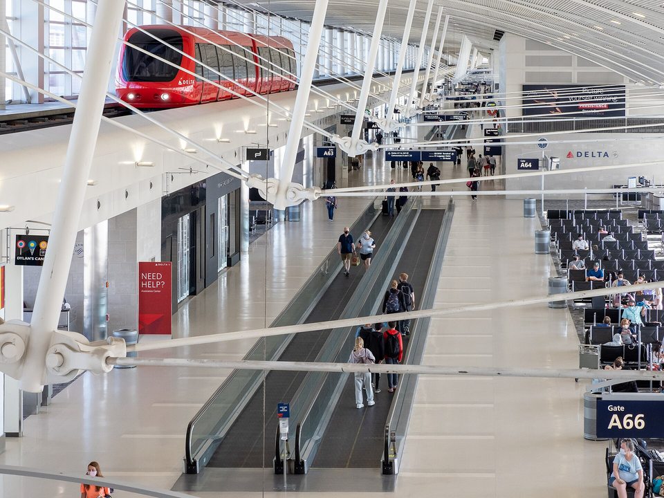 Bright, airy Concourse A of the McNamara Terminal at Detroit Metro Airport, with the red ExpressTram running on its elevated track above moving walkways and gate seating.