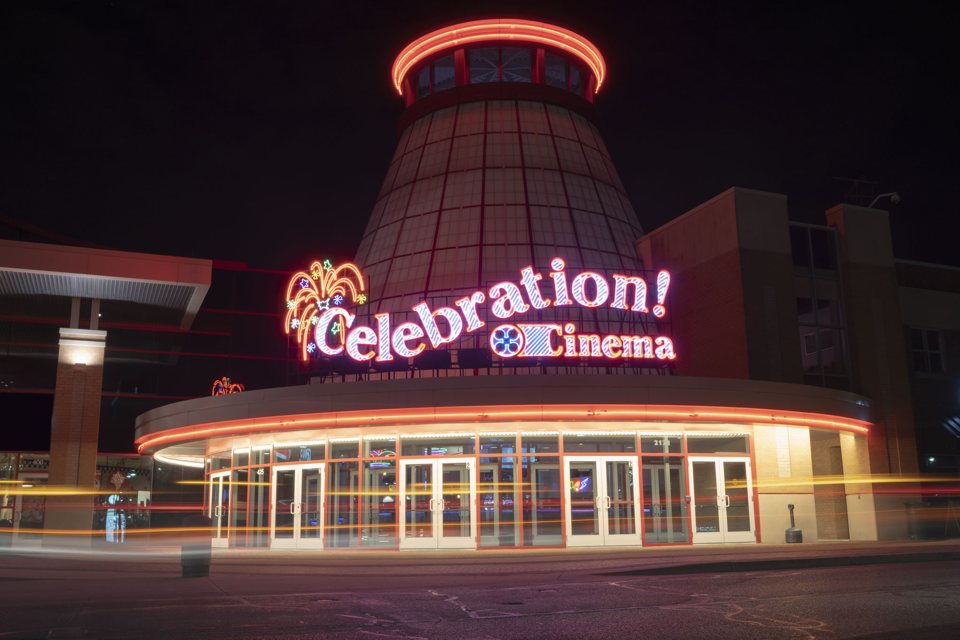 Celebration! Cinema North's cone-shaped tower and curved glass entrance at night, with neon signs and light trails from passing cars