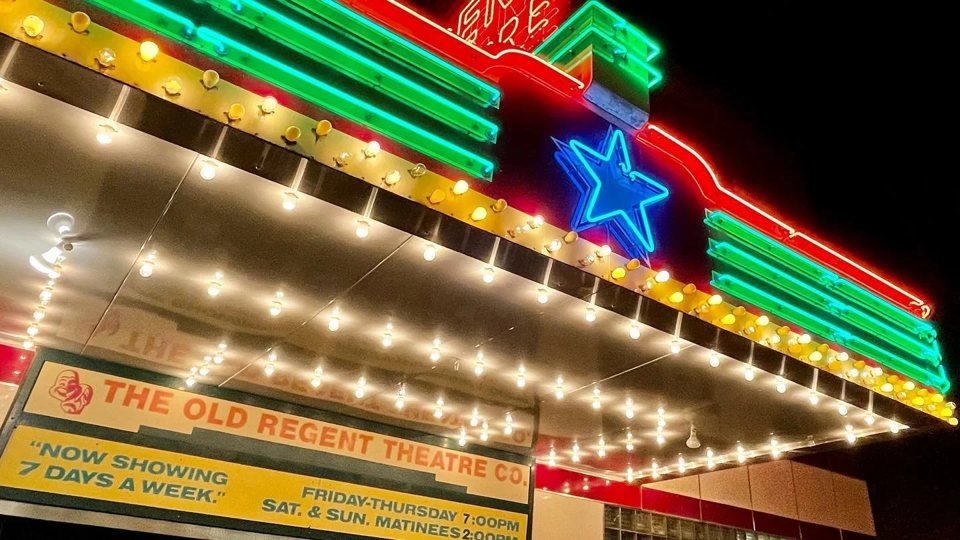 Close-up of the neon and bulb-lit marquee with its blue star and the Old Regent Theatre Company sign