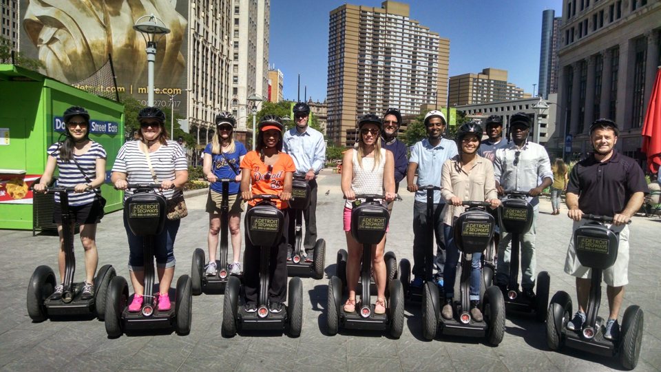 A group on Segways stands in Cadillac Square with downtown Detroit buildings behind them