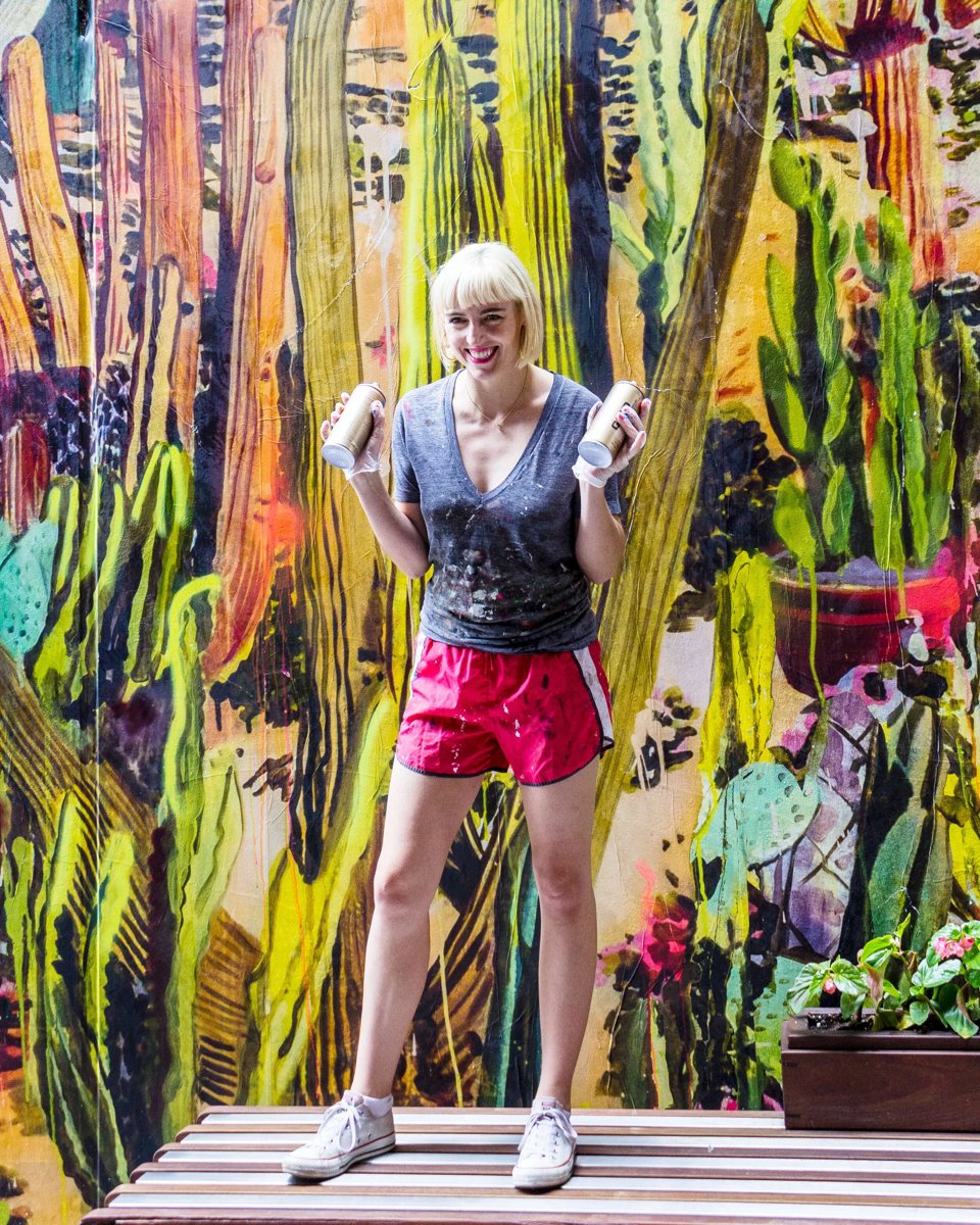 A woman poses in front of a vivid cactus mural in The Belt alley